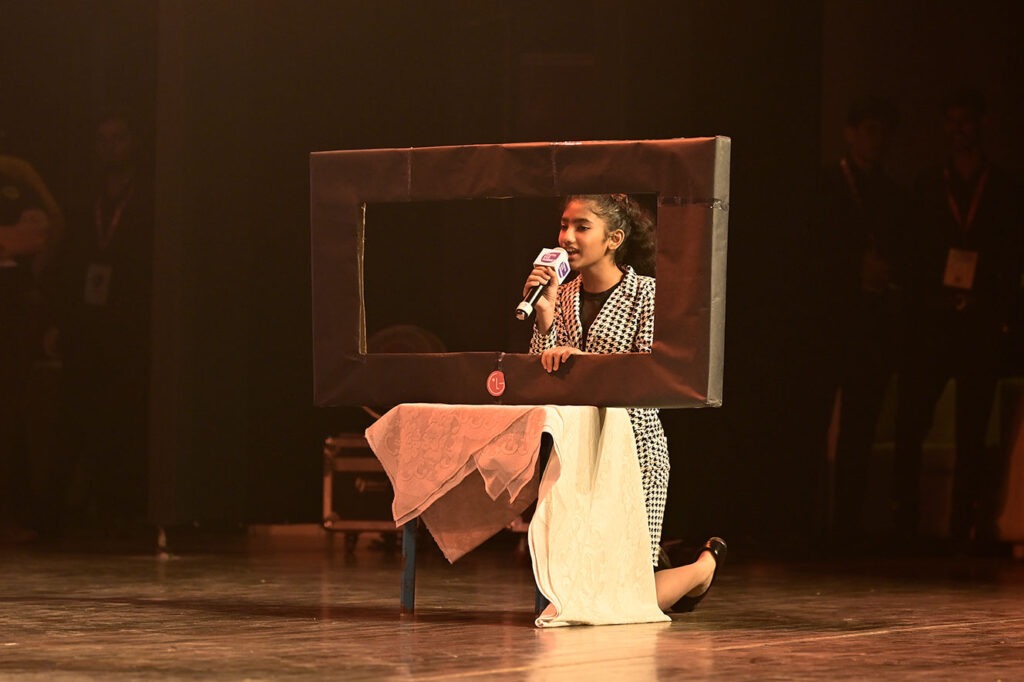 A student speaking into a microphone through a cardboard television prop